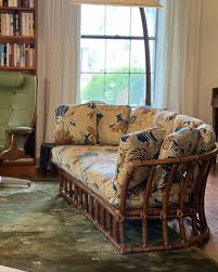 Enhance your space with this charming vintage rattan loveseat, beautifully upholstered in a striking pattern of amber brown, cream, black, and subtle blue tones. The fabric is soft and offers exceptional comfort,