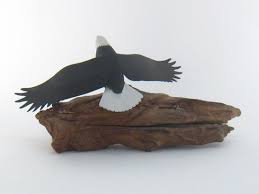 Sold at Auction: A carved and painted wood sculpture of an eagle, wings outstretched, flying above a stripped natural wood form representing a mountain ridge, signed on base "R. Negaard, Park Rapids,